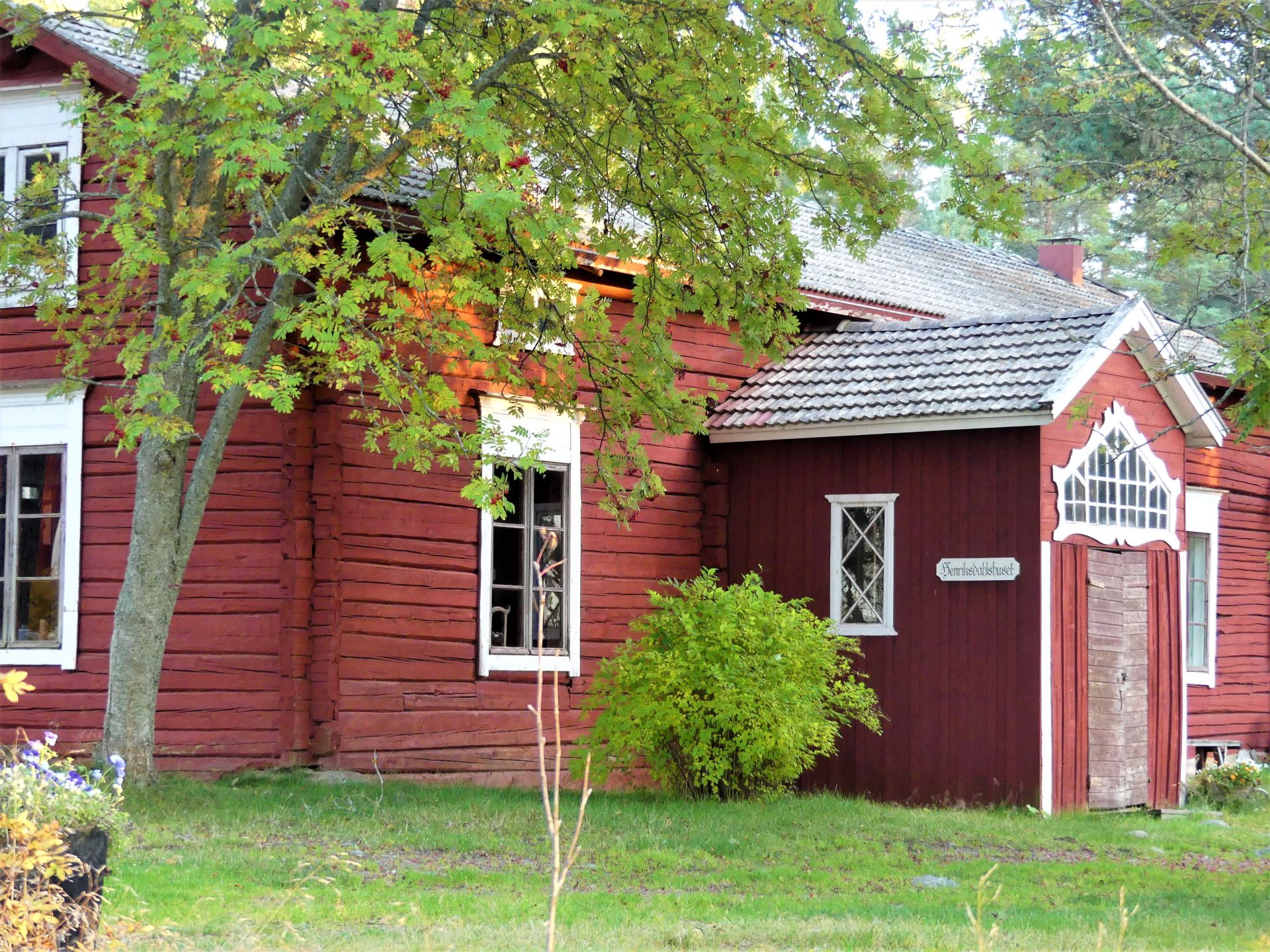 Henriksdalshuset – historisk röd byggnad med skylt, delvis skymd av ett lövträd.