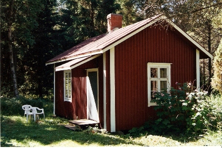 Liten röd stuga omgiven av buskar och träd, tidigare använd av författare.