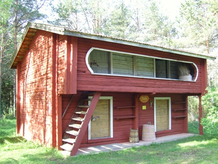 Rött tvåvånings loft med yttre trappa till övre våningen, omgivet av tallskog.
