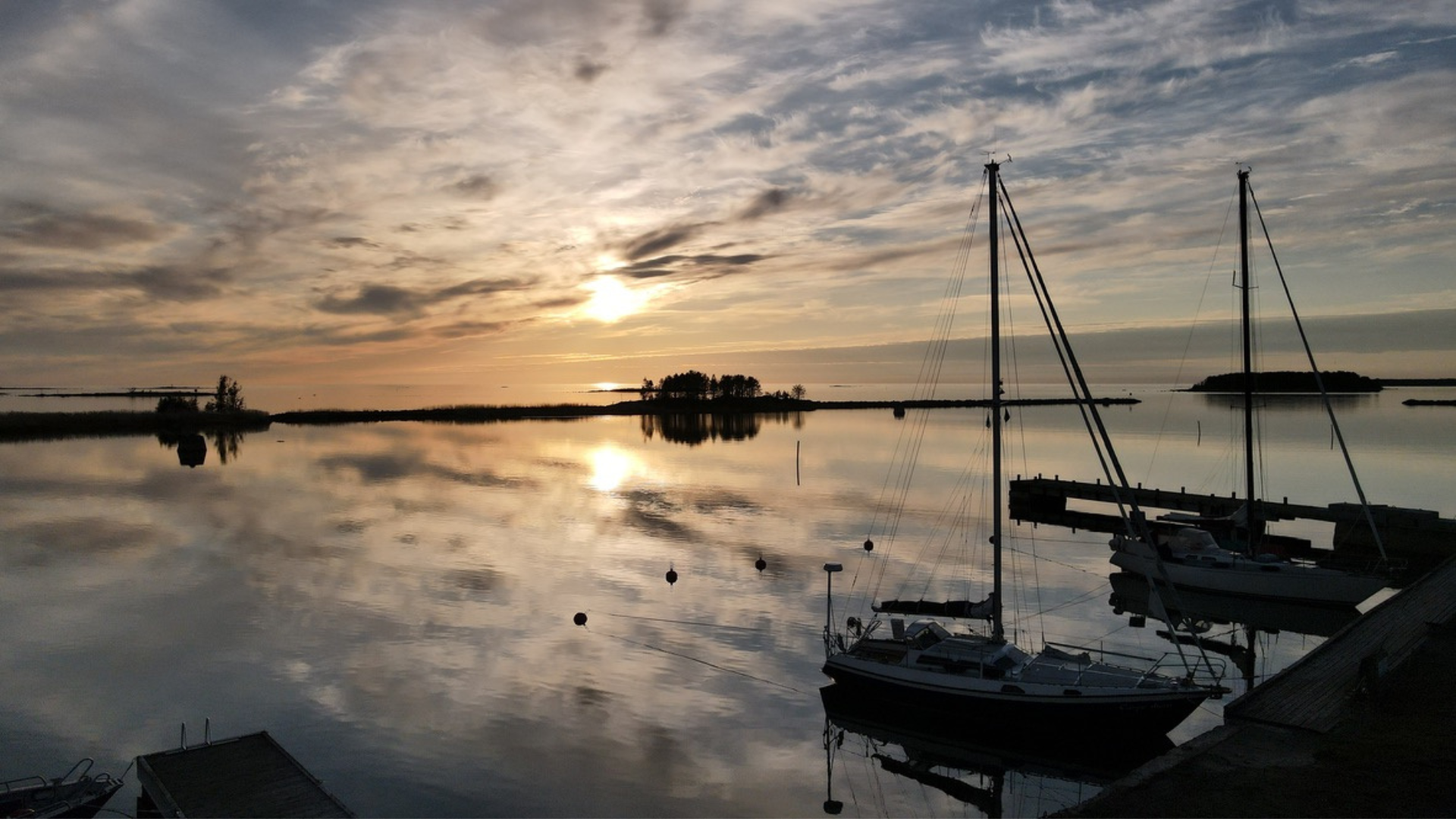 Solnedgång över spegelblankt vatten i Kilens gästhamn med segelbåtar i förgrunden